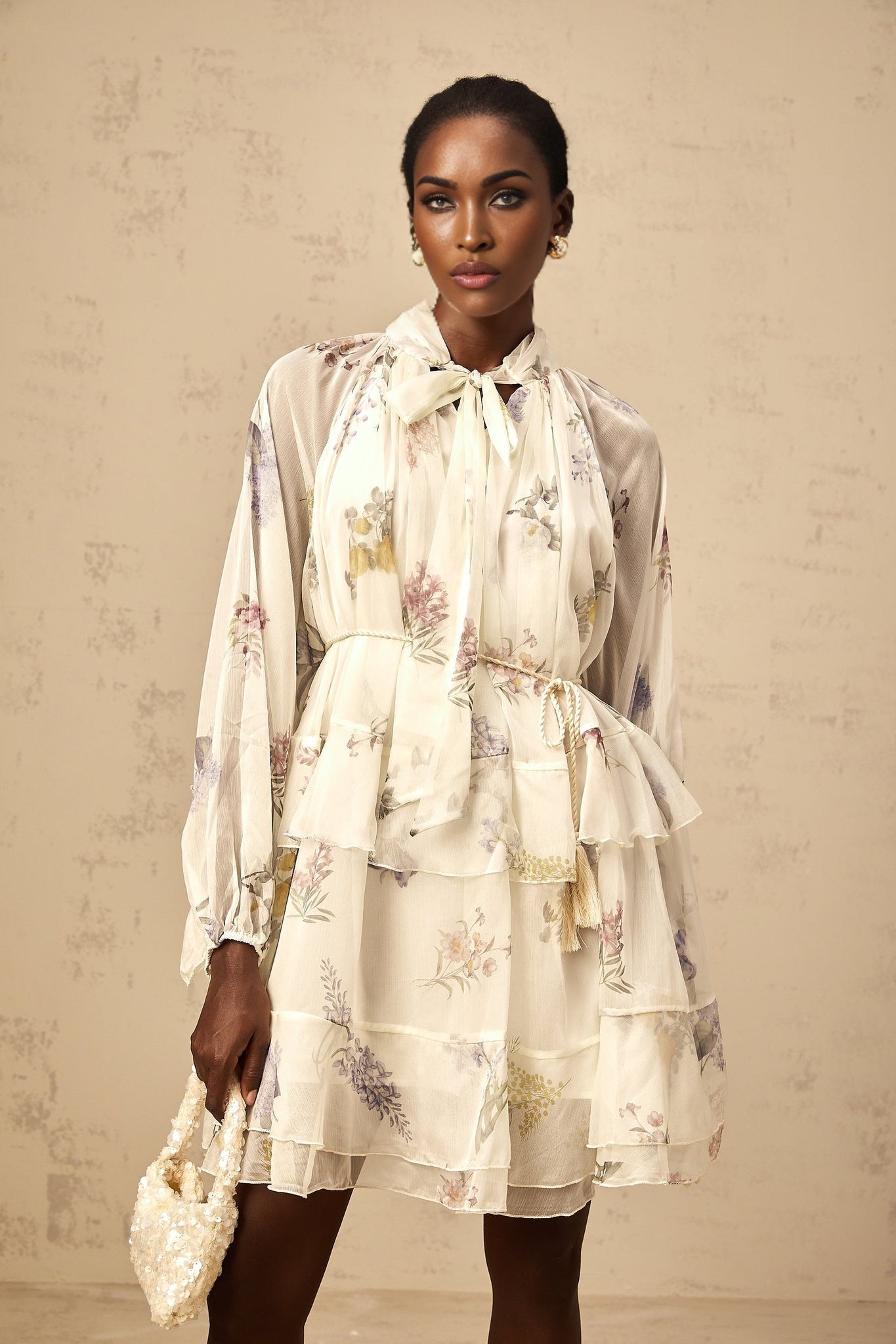 A white mini dress with a floral print pattern made from tiered chiffon fabric featuring a short hemline and lightweight flowing design