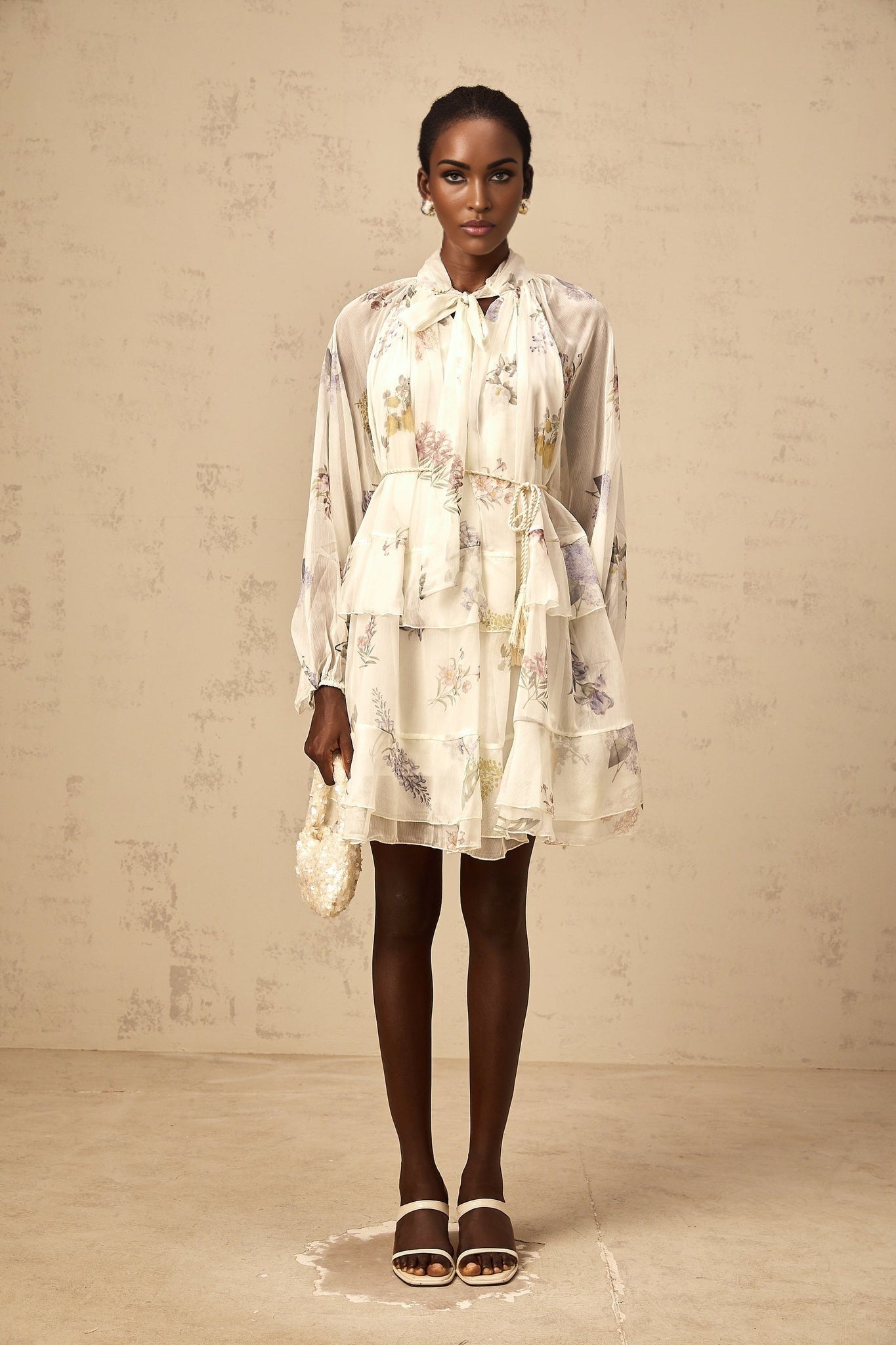 A white mini dress with a floral print pattern made from tiered chiffon fabric featuring a short length and light airy design