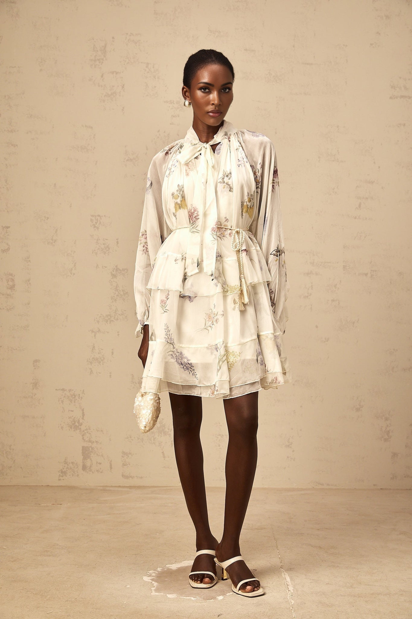 A white mini dress with a floral print pattern made of tiered chiffon fabric featuring a short length and light airy design