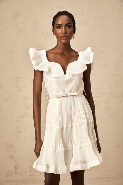 A white mini dress with a frilled neckline and pleated skirt worn by a model against a plain background