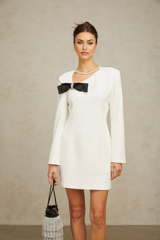 A white mini dress with an asymmetric hemline featuring a bowknot detail and named Colette