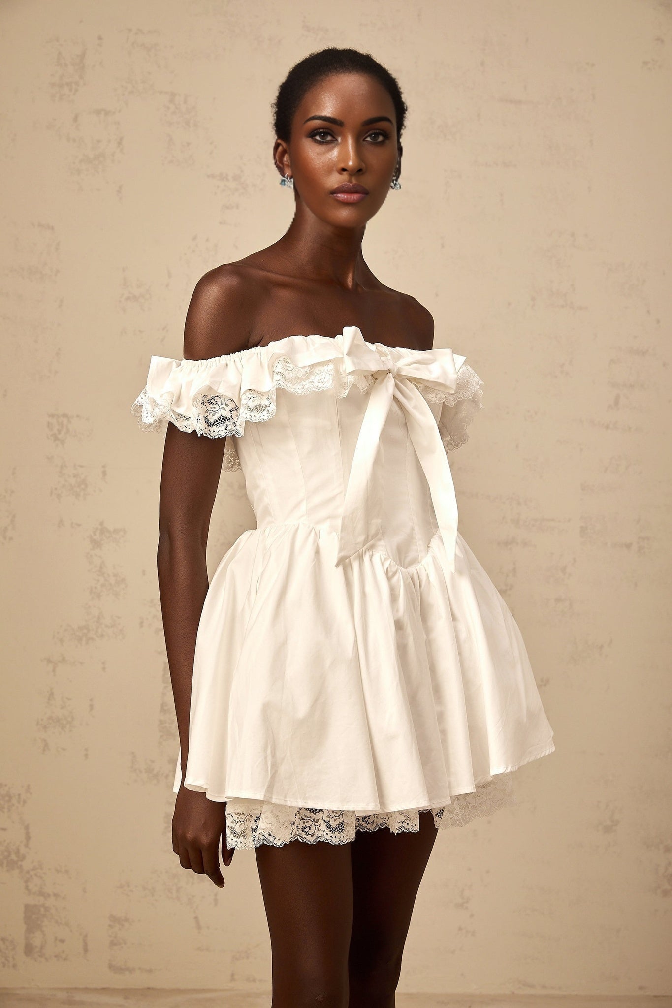 A white mini dress with an oversized bow and ruffled details featuring a short hemline and loose fitting silhouette