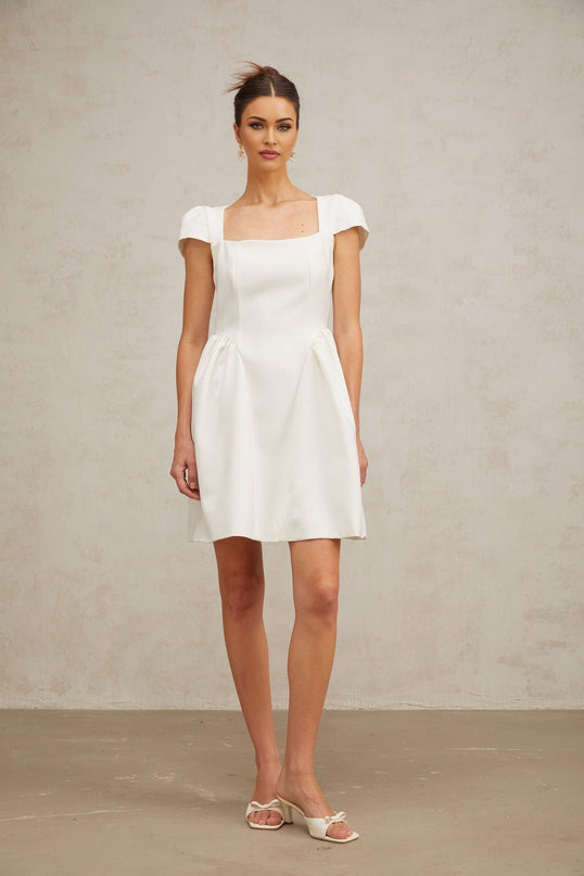 A white mini dress with cap sleeves featuring a fitted bodice and a flared skirt worn by a model against a plain background