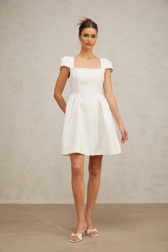 A white mini dress with cap sleeves featuring a fitted silhouette and short hemline The dress has a clean simple design with a feminine look suitable for summer or formal occasions