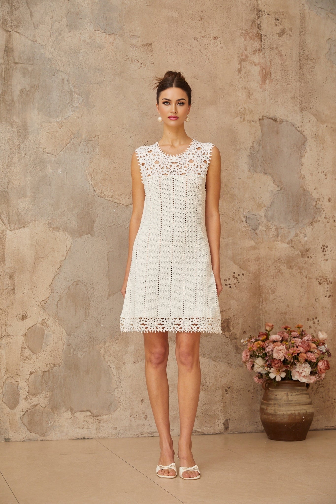 A white mini dress with floral applique detailing and crochet knit texture featuring short sleeves and a fitted silhouette