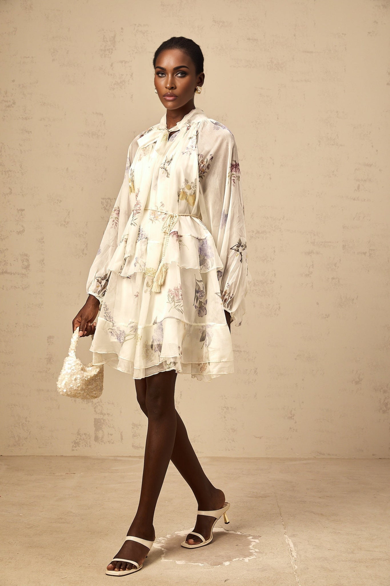 A white mini dress with floral print pattern made of tiered chiffon fabric featuring a short hemline and lightweight flowing design