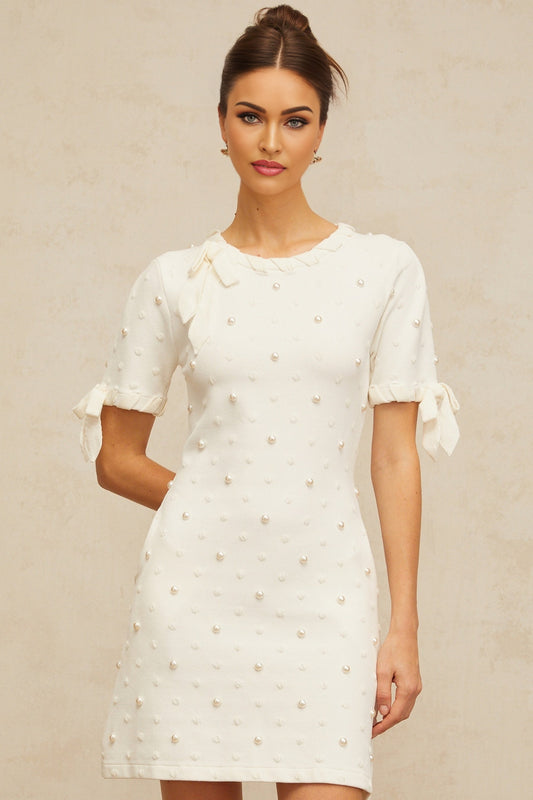 A white mini dress with polka dot pattern and heart design knitted into the fabric featuring a short hemline and Prunelle branding