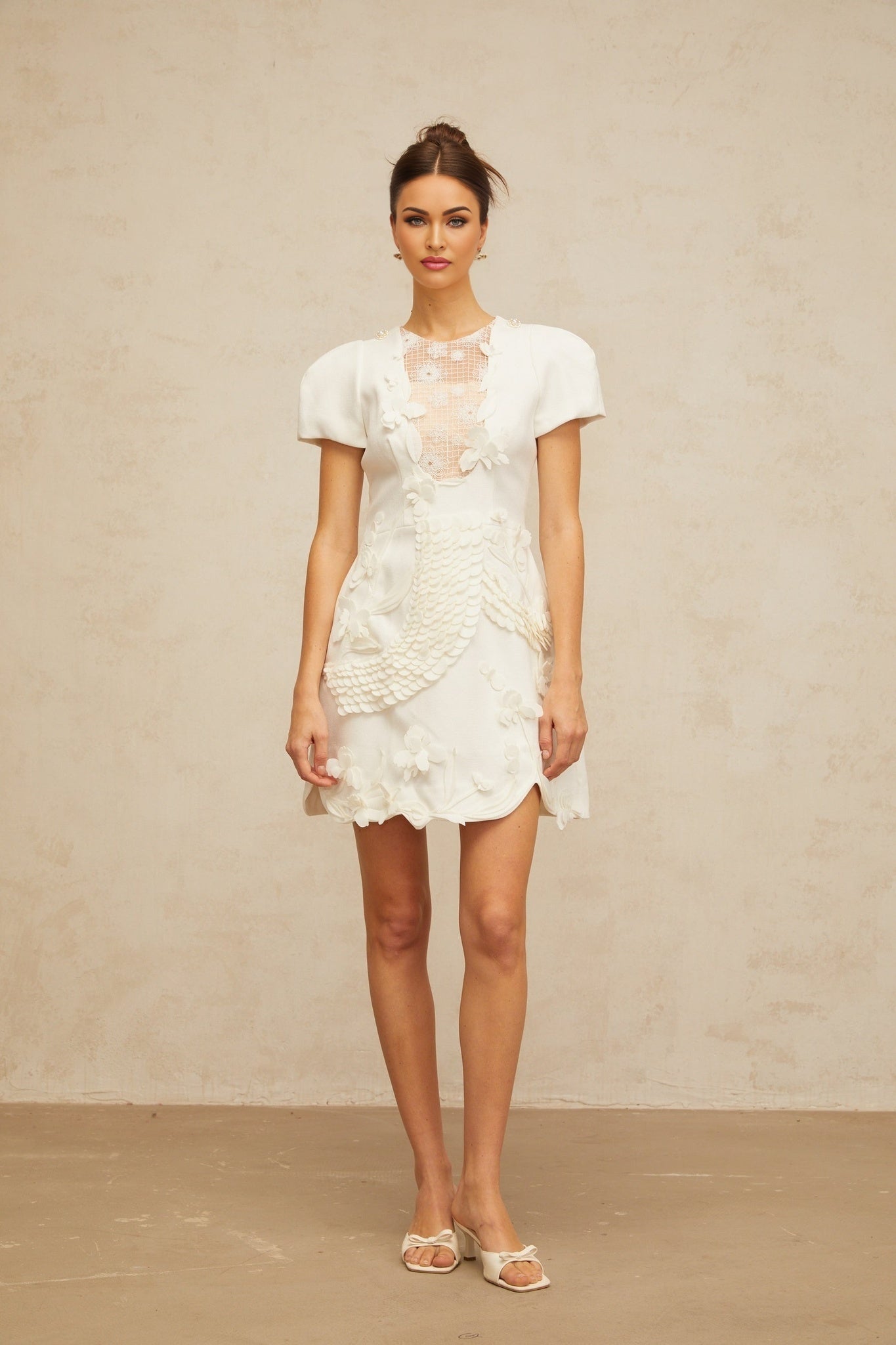 A white mini dress with puffed sleeves and floral applique details featuring a feminine silhouette and delicate floral embellishments