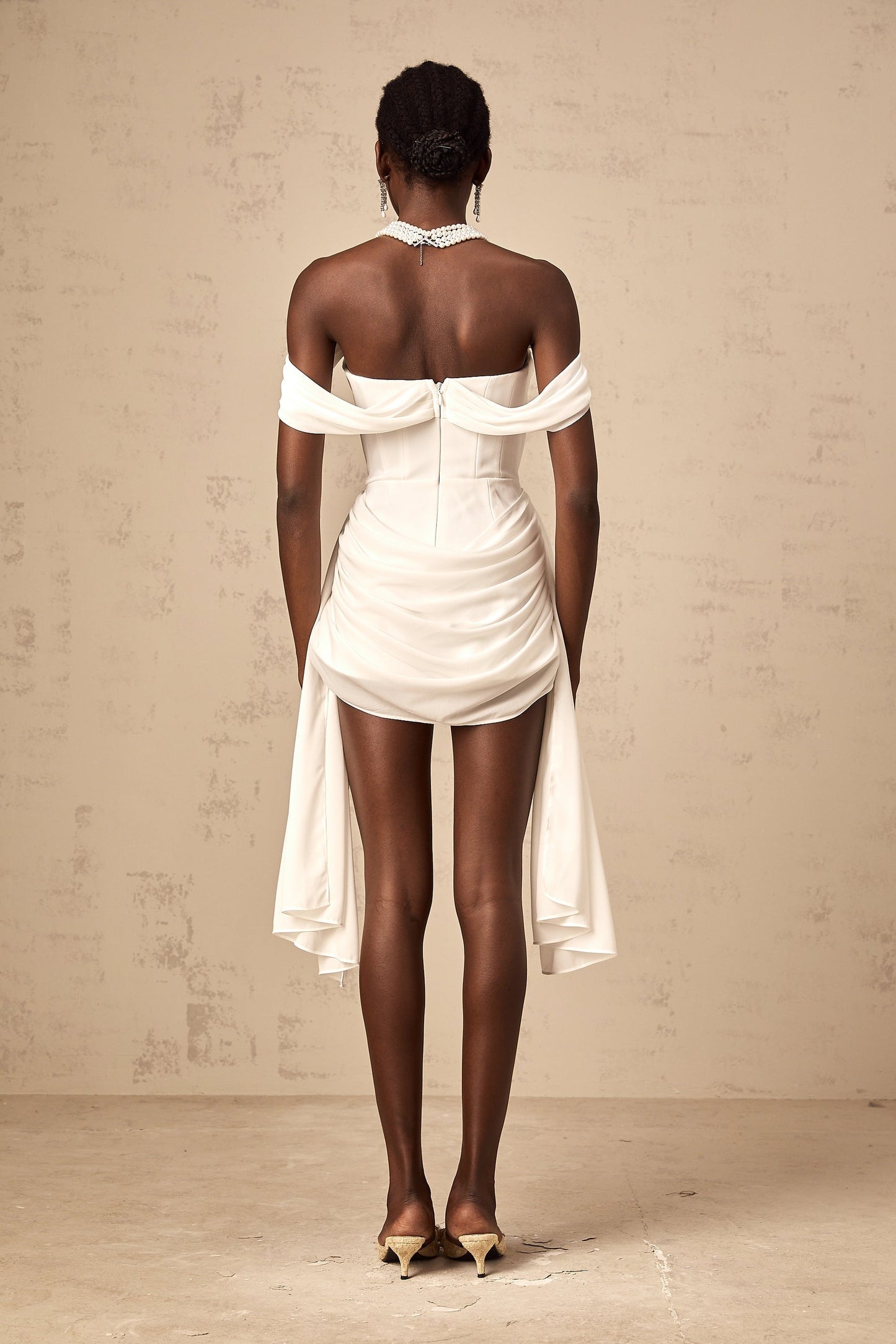 A white mini dress with ruched fabric and ribbon design details featuring a short hemline and formfitting silhouette