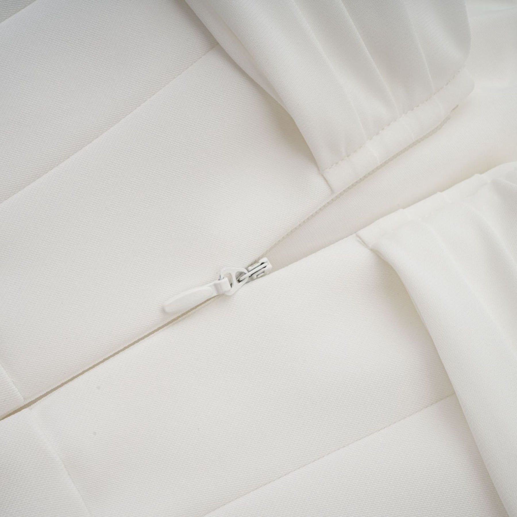 A white mini dress with ruched fabric and ribbon design details worn by a model against a plain background