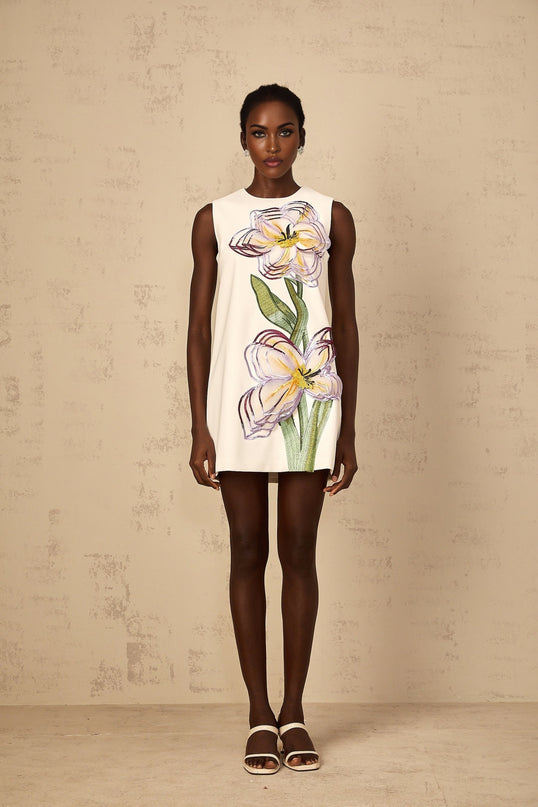 A white mini dress with sequin floral embroidery detail worn by a female model standing against a plain background