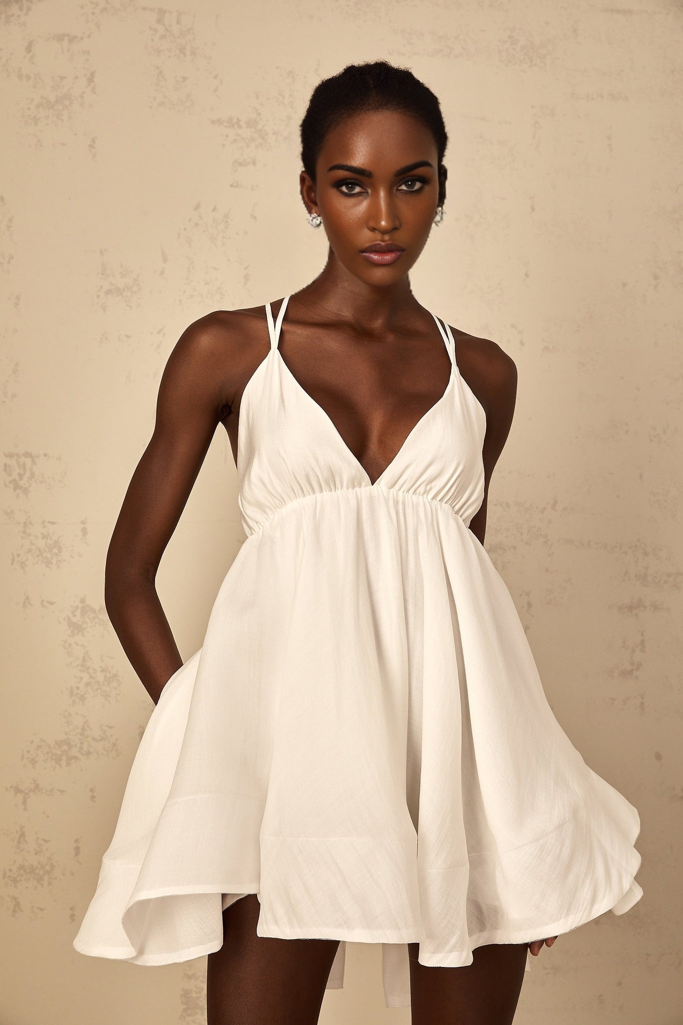A white mini dress with shirred detailing and a flounced hem featuring a feminine and playful design suitable for summer occasions