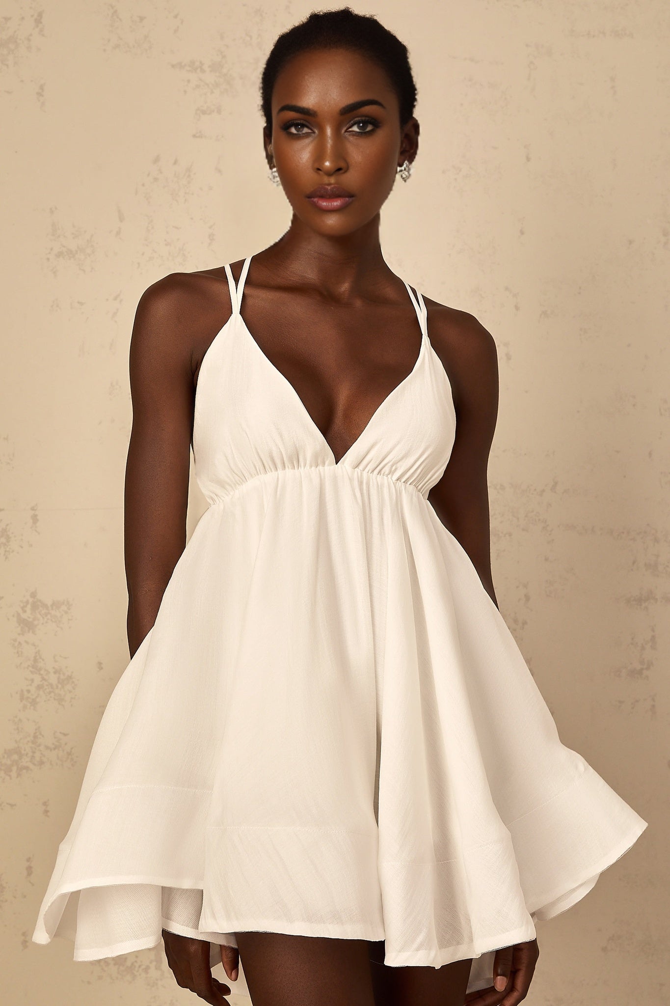 A white mini dress with shirred detailing and a flounced hem featuring a feminine and playful design