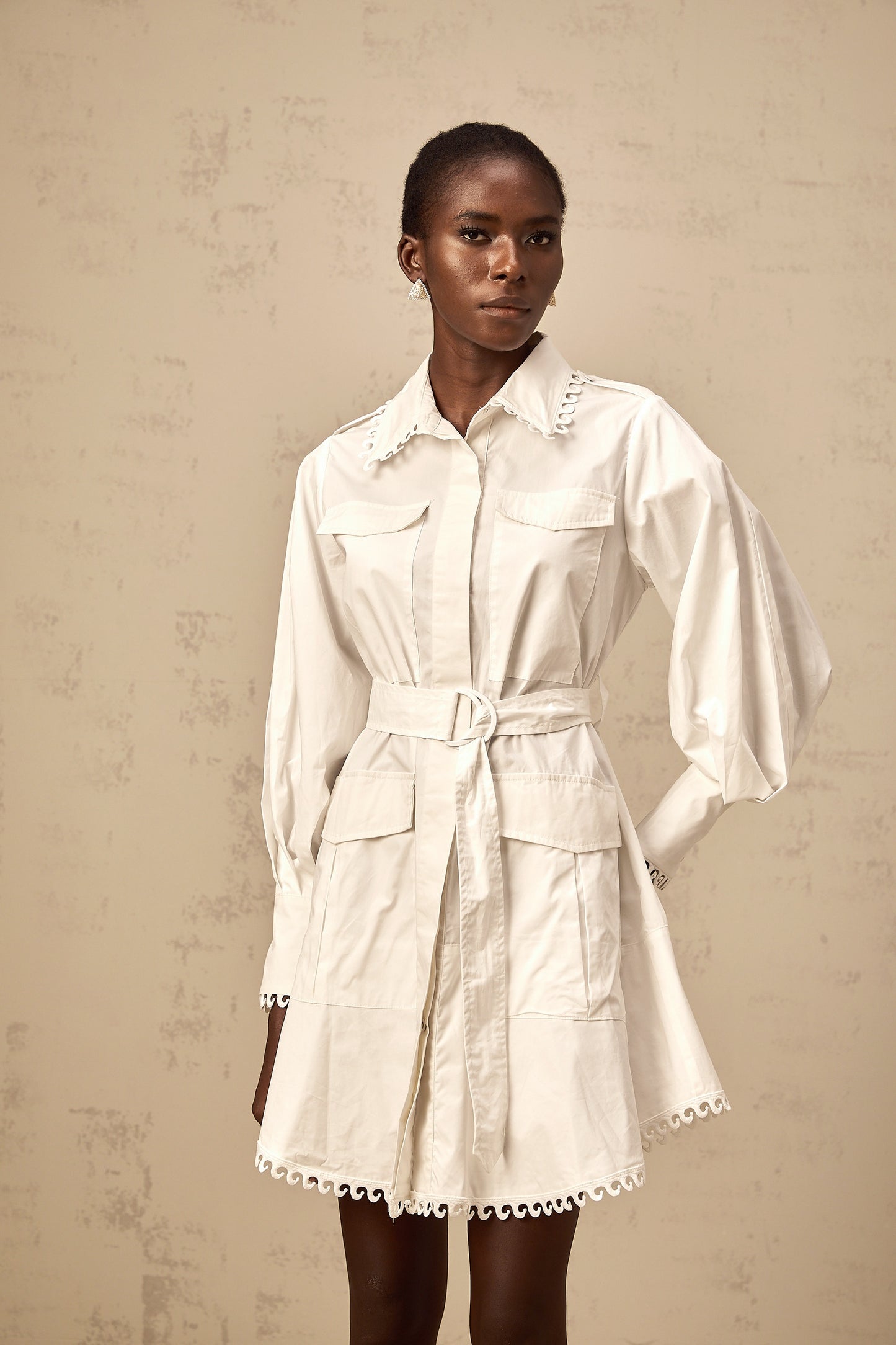 A white mini shirt dress with a belt cinched at the waist featuring short sleeves and a collar