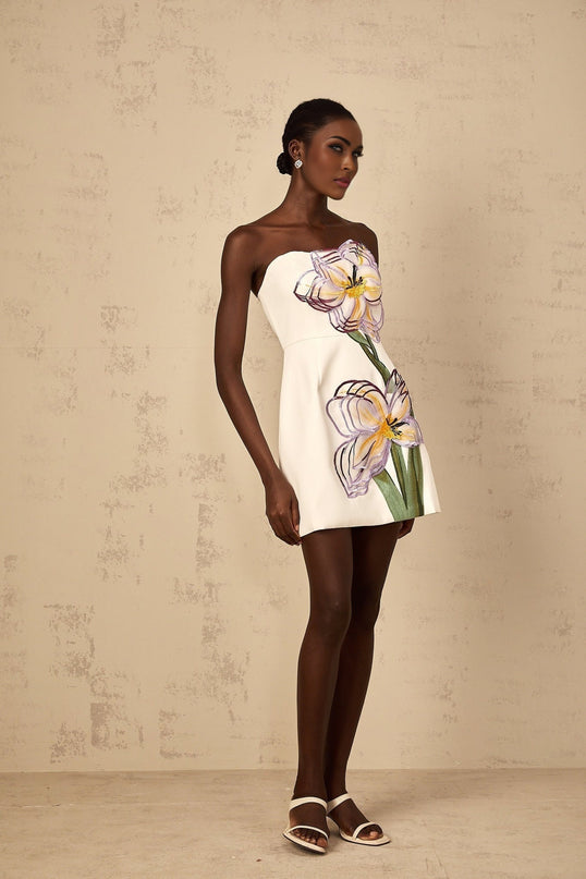 A white off shoulder mini dress with sequin and floral embroidery details worn by a woman
