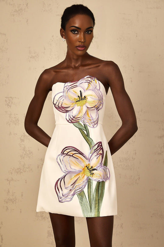 A white off shoulder mini dress with sequin floral embroidery worn by a female model standing against a plain background