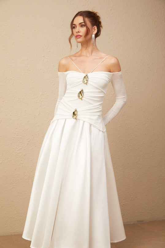 A white offshoulder maxi dress with panel detailing worn by a model standing against a plain background