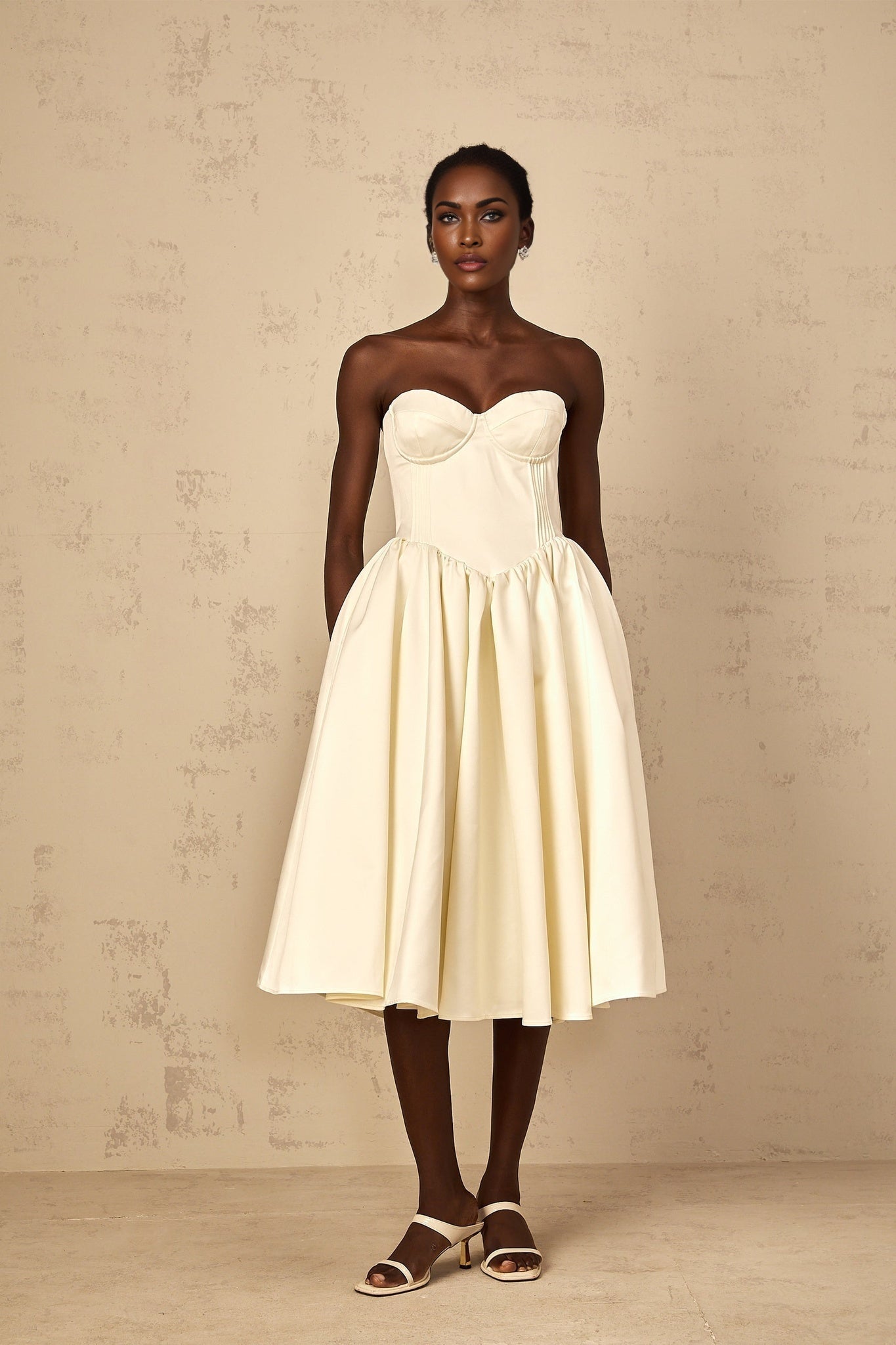 A white offshoulder midi dress with shirred details worn by a woman standing against a neutral background