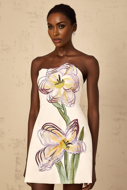 A white offshoulder mini dress with sequin floral embroidery worn by a woman against a plain background
