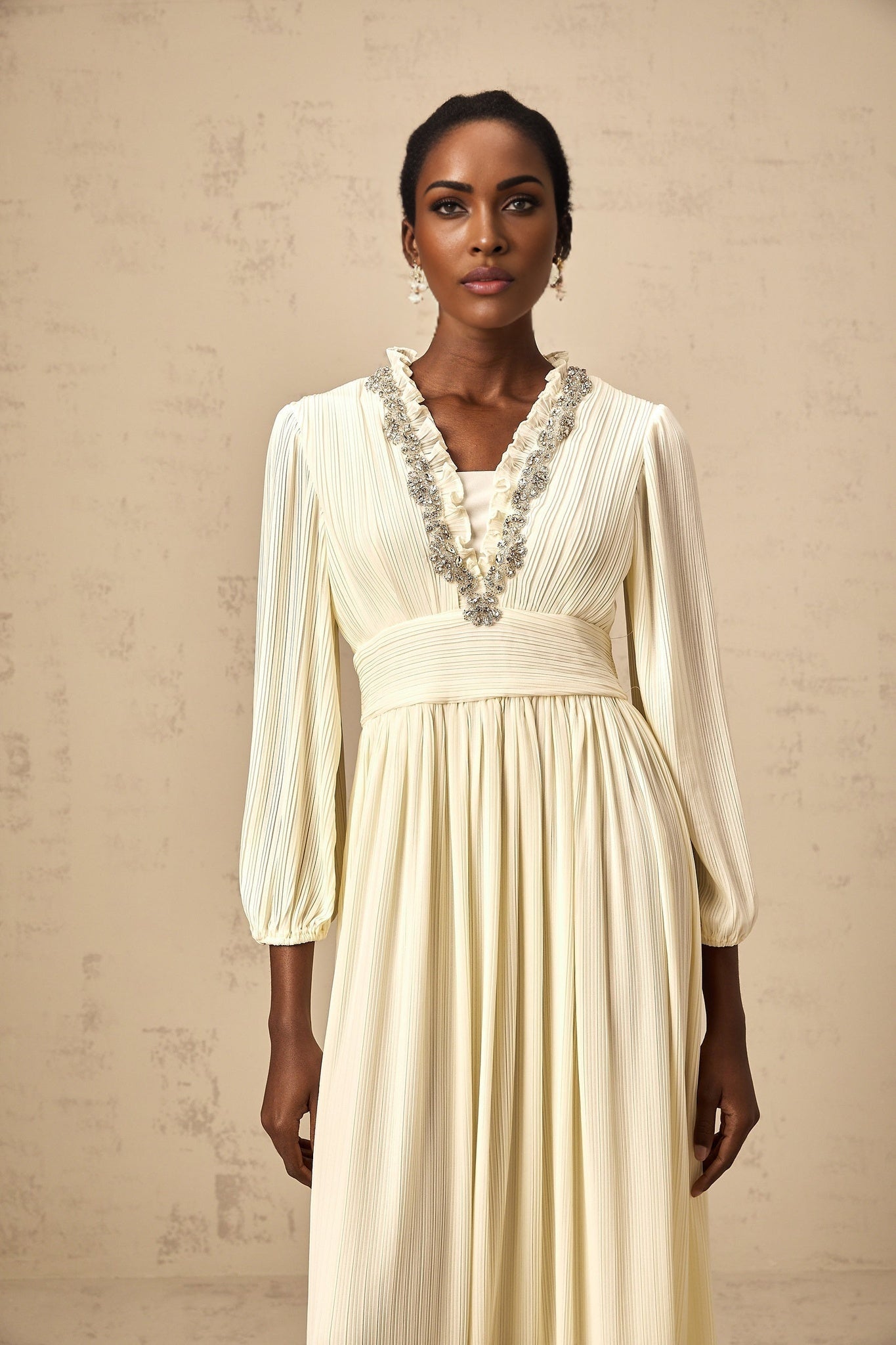 A white pleated midi dress with crystal trim details along the neckline and waist featuring a flattering silhouette and delicate embellishments