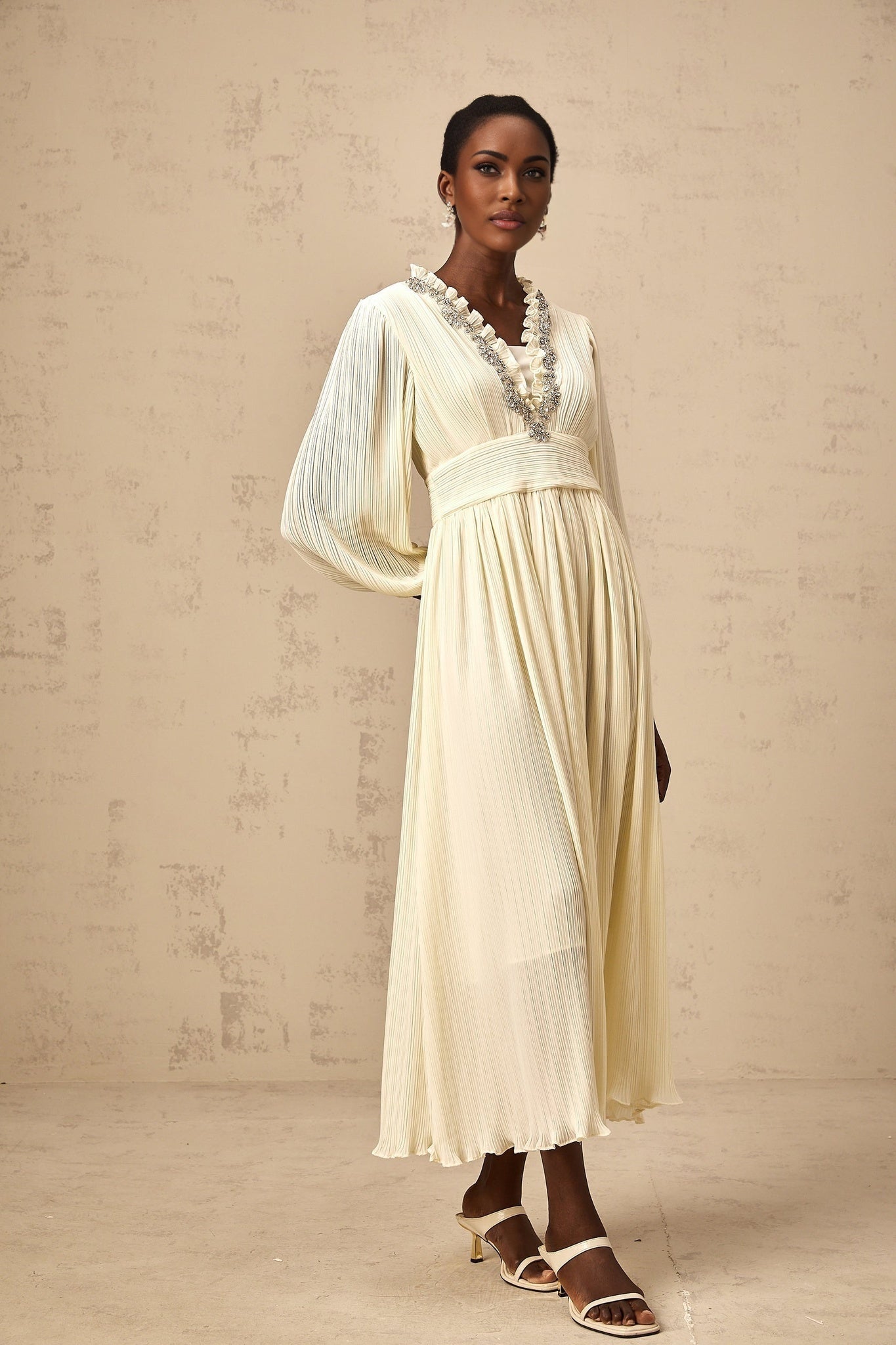 A white pleated midi dress with crystal trim details along the neckline and waist named Yana