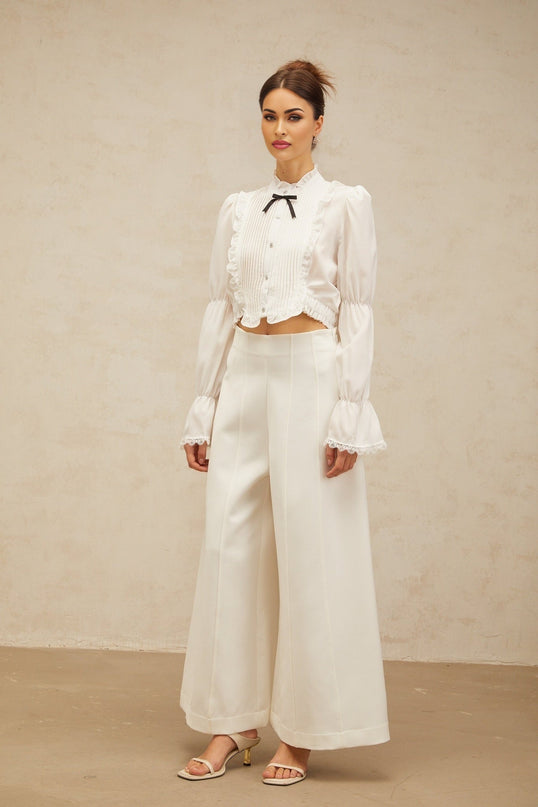 A white ruffled shirt with a bow knot detail and shirred panels featuring a feminine design and delicate texture