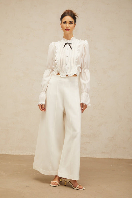 A white ruffled shirt with a bow tie detail and shirred panels featuring a feminine and elegant design