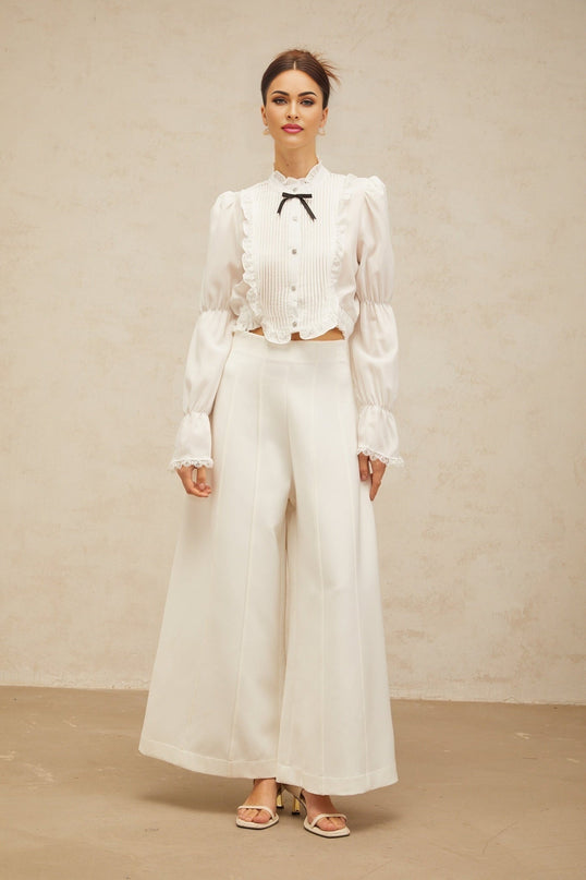 A white ruffled shirt with a bow tie neckline and shirred panels featuring a feminine and elegant design