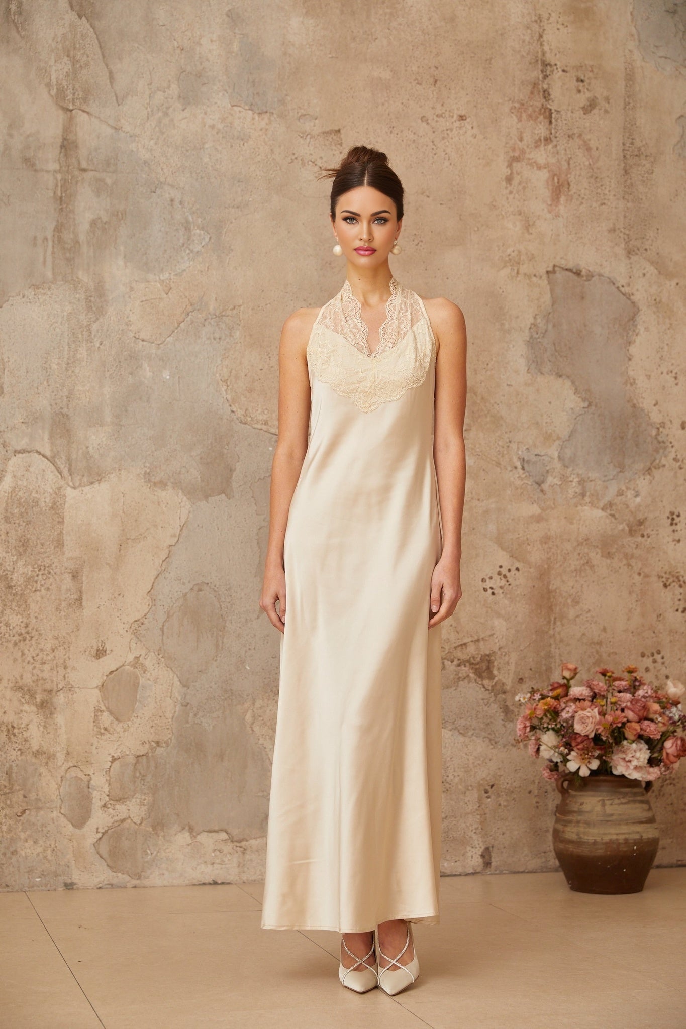 A white satin maxi dress for women with lace trim details worn by a model standing against a plain background