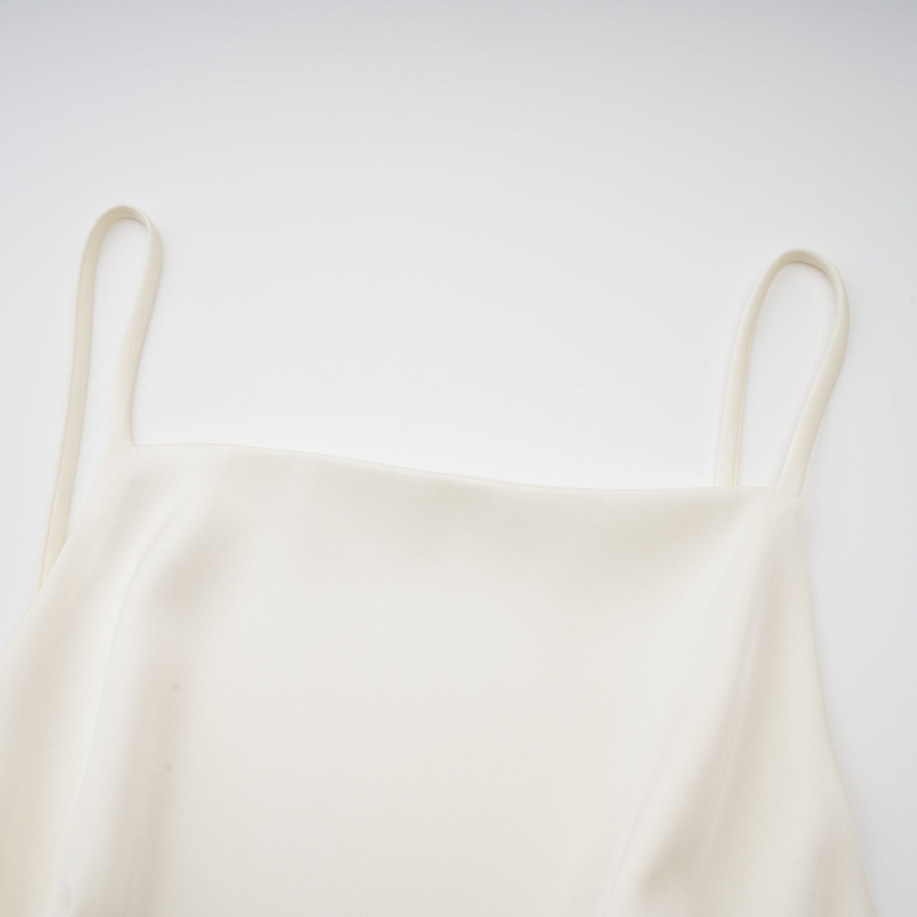 A white satin mini dress with ruffled details and a shawl panel worn by a model against a plain background