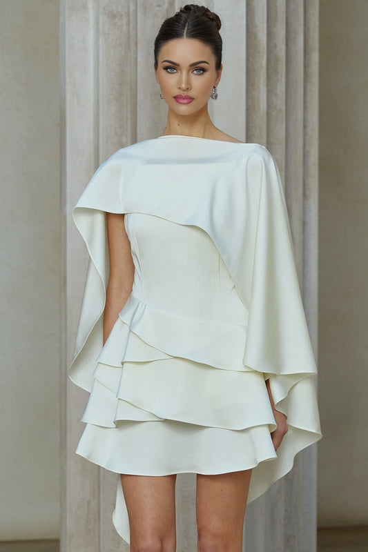 A white satin mini dress with ruffled details and a shawl panel worn by a model standing against a plain background
