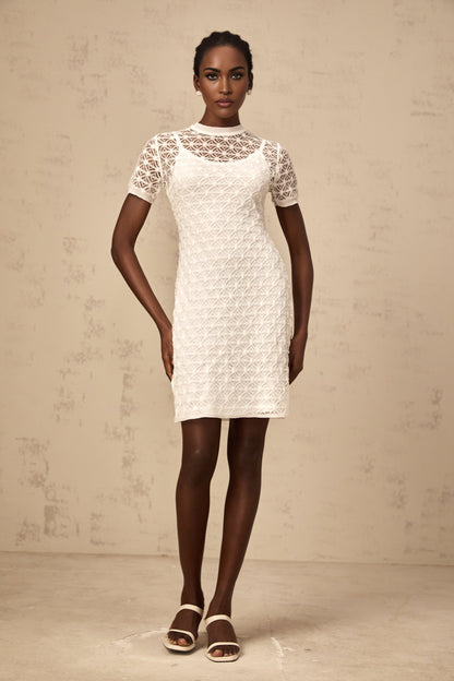 A white semisheer knit mini dress on a model against a plain background showcasing the dresses short length and delicate fabric texture
