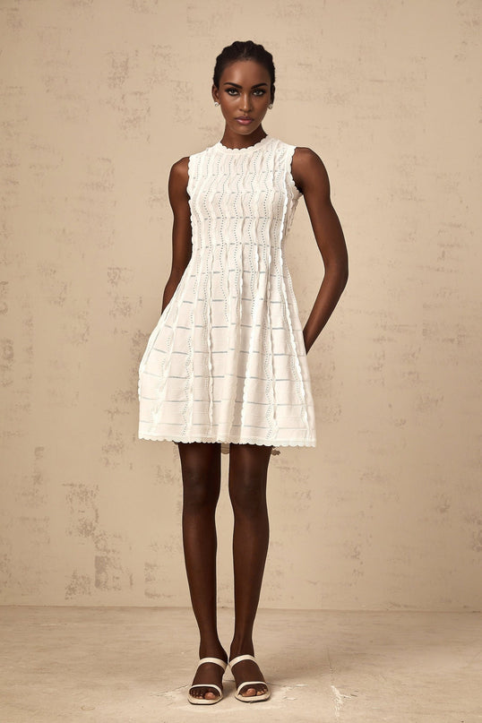 A white sleeveless knit mini dress with ruffled details featuring a fitted silhouette and short hemline