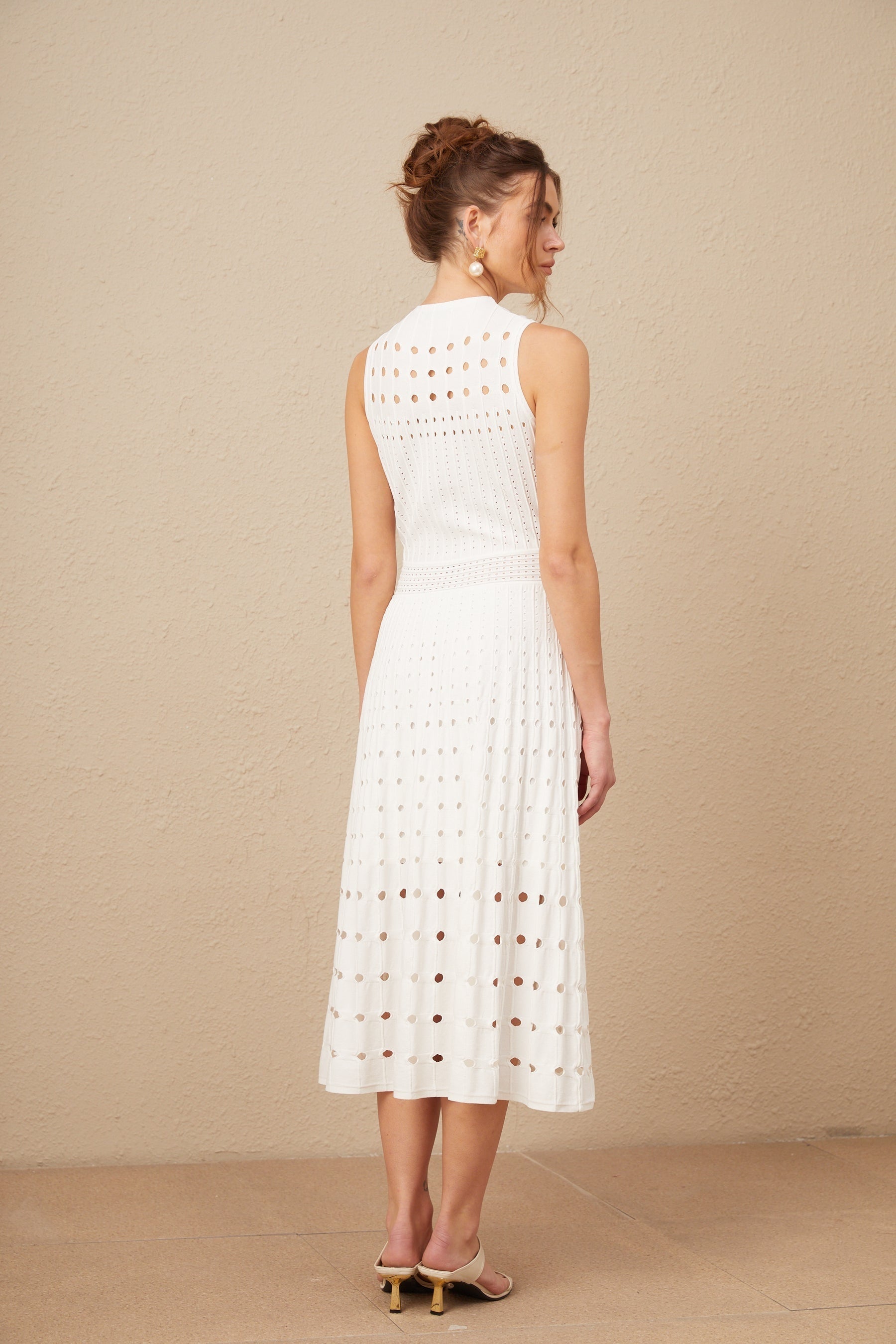 A white sleeveless knitted midi dress with cut out details modeled on a woman against a plain background