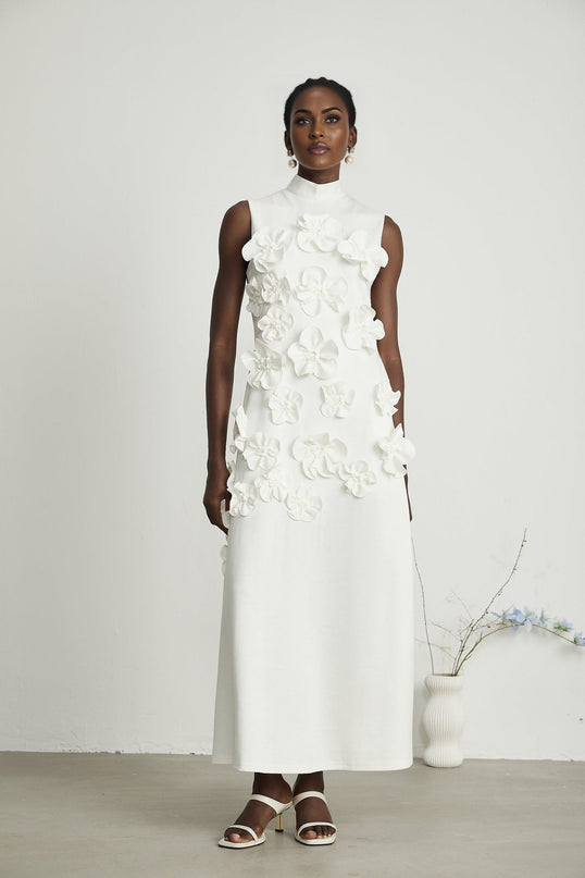 A white sleeveless maxi dress named Magali with a bow detail and decorative artificial flowers