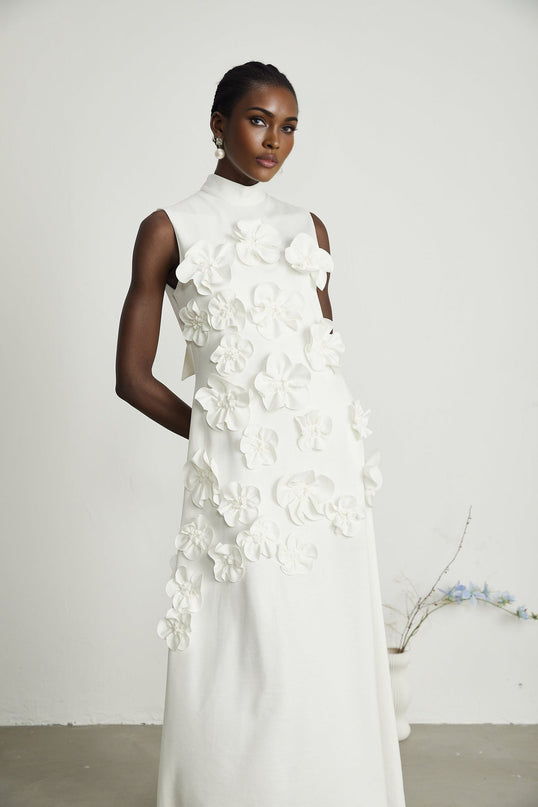 A white sleeveless maxi dress with a bow and artificial flower embellishments named Magali