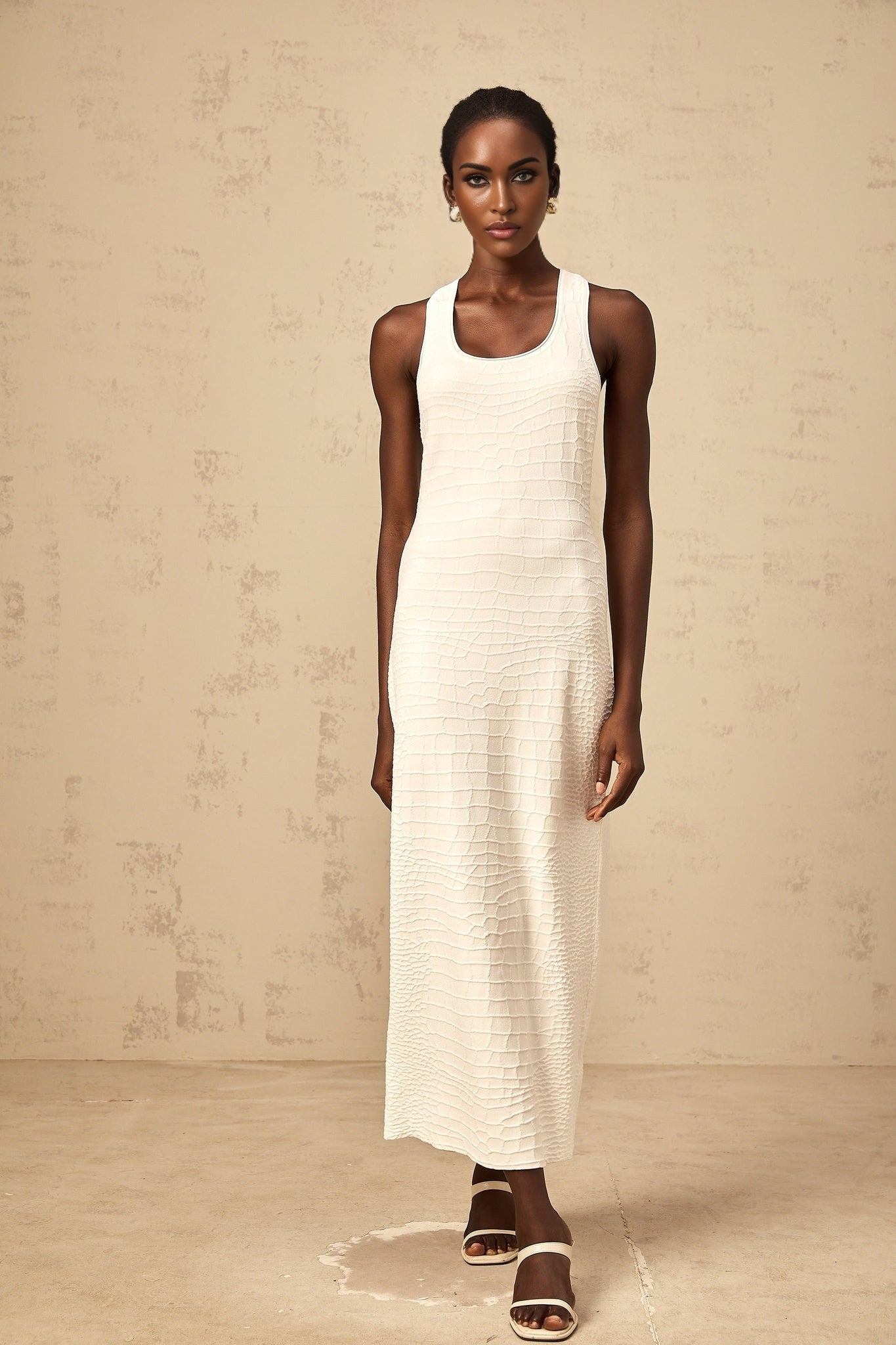 A white sleeveless midi dress with a textured jacquard pattern worn by a woman standing in a neutral background