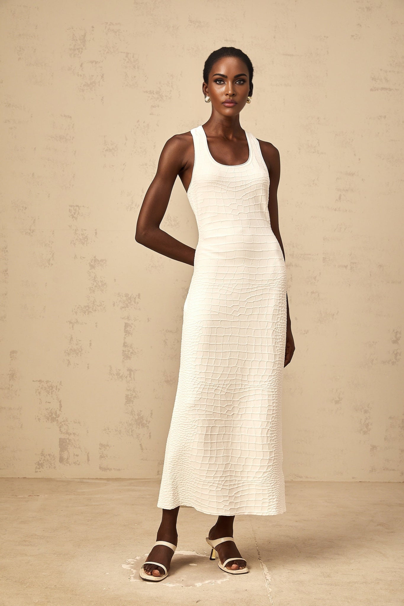 A white sleeveless midi dress with a textured jacquard pattern worn by a woman standing in a neutral setting