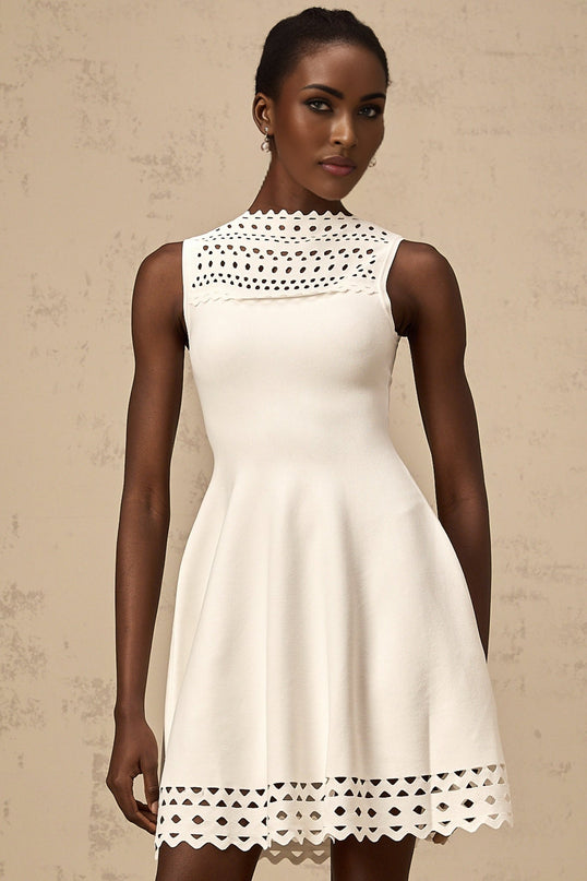 A white sleeveless mini dress with a knitted texture and cutout details worn by a model standing against a plain background