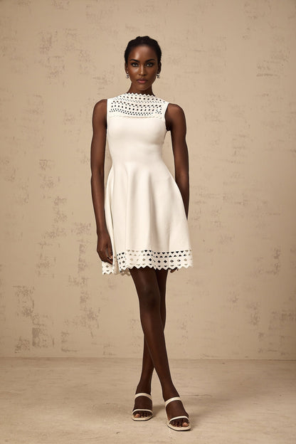 A white sleeveless mini dress with cutout details and a knitted texture featuring a formfitting silhouette