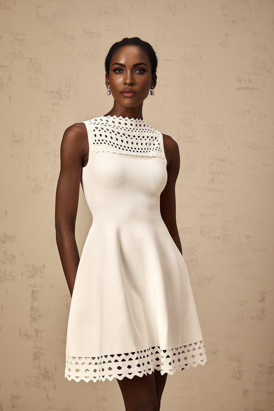 A white sleeveless mini dress with knitted fabric and cutout details worn by a model standing against a plain background