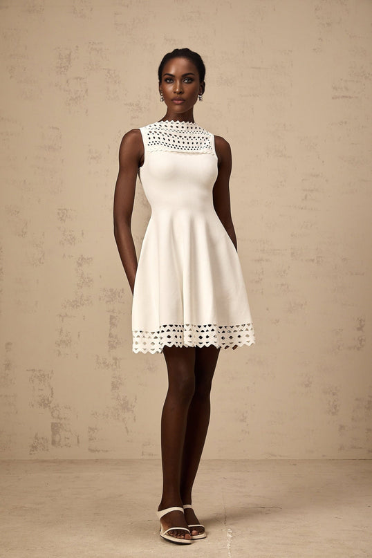 A white sleeveless mini dress with knitted fabric and cutout details worn by a model