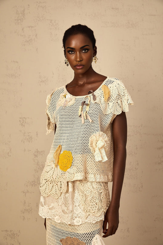 A white sleeveless top with a delicate lace panel and crochet knit pattern featuring intricate details and a feminine design