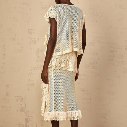 A white sleeveless top with delicate lace panels and crochet knit design featuring a scalloped neckline and intricate floral patterns