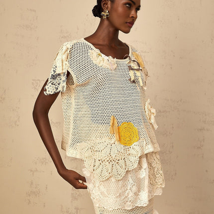 A white sleeveless top with intricate lace panels and crochet knit detailing featuring a scoop neckline and delicate feminine design