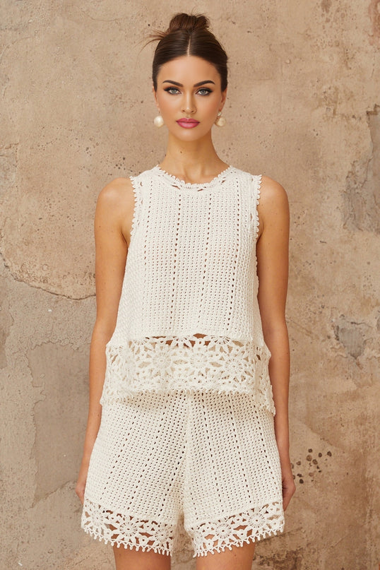 A white two piece outfit consisting of a crochet knit top and shorts adorned with floral applique details