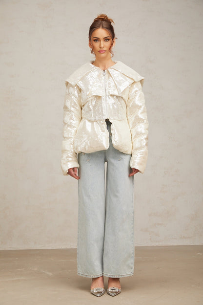 A white winter coat with sequin embellishments and down insulation featuring a woman named Joslyn wearing the garment