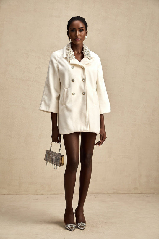 A white woolen coat with embellishments named Fabienne hanging on a display