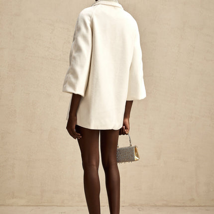 A white woolen coat with embellishments named Fabienne hanging on a display