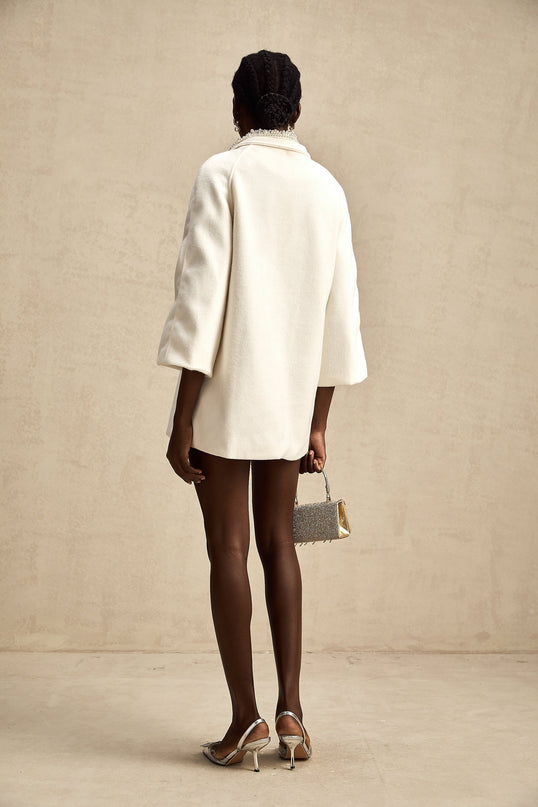 A white woolen coat with embellishments named Fabienne hanging on a display